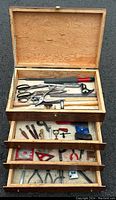 Full view of wooden box lid open showing several tools including scissors, pliers, rulers, and boxes inside drawers.