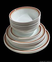 Stack of white dishes with brown and orange striped rim pattern including bowls and various sized plates.