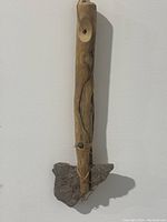 Front view of the stone axe head attached to a carved wooden handle with natural twine tied for securing the stone.