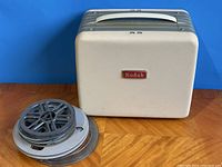 Front view of the Kodak Brownie 500 projector in its closed carrying case next to two film reels, one silver and one gray plastic.