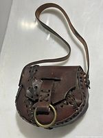 Front view showing the leather lacing detail, flap closure with a metal ring, and the shoulder strap.