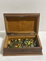 Open wooden box showing collection of assorted glass marbles inside, felt lining visible