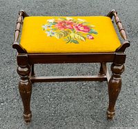 Front view of vintage wooden bench with yellow floral needlepoint seat showing turned legs.