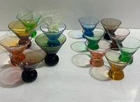 Photo showing 14 vintage colored glass shot glasses arranged in two groups, highlighting the variety of colors and classic depression era glass shape.