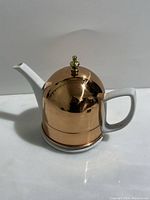 Tea pot showing copper outer sleeve with brass knob on top and white ceramic exposed handle and spout