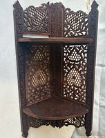 Front view of vintage wooden corner shelf showing two triangular shelves and intricate ornate lattice carved wood panels on back and sides.