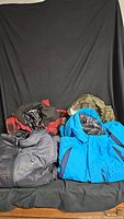 Four winter jackets displayed together in black, blue, red plaid, and green colors showing variety in style and size.