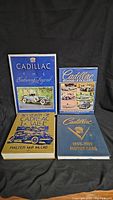 Four hardcover books about Cadillac history arranged on black background, showing front covers with titles and imagery.