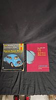 Front covers of two automotive repair manuals placed side by side on a black background. Left book is VW Beetle & Karmann Ghia Haynes Repair Manual 1954-1979 with a blue Beetle rear image. Right book is The 1949-1959 VW Beetle with a red cover showing a blue Beetle.