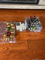 Photo shows 3 packs of Christmas balls in gold, red, green, silver, black, and purple colors, and 2 clear plastic trays with white and multicolor snowflake ornaments