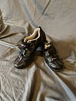 Pair of black Louis Garneau cycling shoes with pink and white detailing, showing top and side views on grey cloth background.