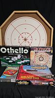 Shows several boxed games including Othello, DaVinci's Challenge, Trouble, and Daytona Challenge with a circular wooden Croconole/checkers board behind them.