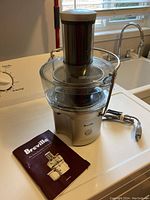 Breville Juice Fountain Compact juicer with power cord and instruction manual laid out on surface.