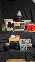 Full view of the darkroom equipment collection with Vivitar PTC enlarger lit up, various film tanks, trays, timers, and boxed chemicals visible