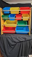 Full front view of the toy shelving unit showing all colorful bins on the wooden frame.