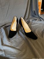 Front view of black velvet Manolo Blahnik heels placed on gray fabric background.