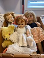 Box containing three vintage dolls and one yellow teddy bear seen from the front