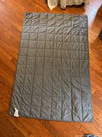 Full view of the grey weighted blanket laid flat on a hardwood floor, showing quilted square pattern.