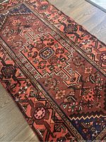 Top-down angled shot of salmon-colored handmade Persian Zanjan rug with detailed geometric and floral patterns in navy and brown on hardwood flooring.