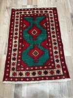 Full rug laid flat showing geometric diamond and triangular shapes in red, green, cream, and black.