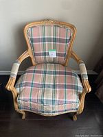 Front view showing carved wood frame and plaid padded upholstery of the armchair.