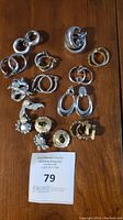Full lot of clip on earrings laid out on wooden table showcasing various silver toned and decorated styles.