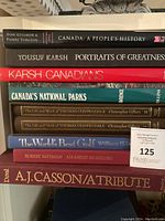 Photo showing spines of 9 assorted coffee table books focusing on Canada, art, and golf including works by Yousuf Karsh, Robert Bateman, and A.J. Casson.