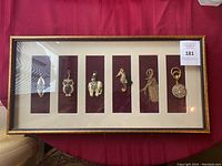 Framed gold-colored decorative pins arranged on dark red background mat in gold frame