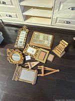 Overview of all golden decorative items laid out on dark floor, includes various frames, a mirror, and golden bookends.