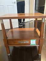 Front view of solid wood side table showing drawer and wood legs with metal caps.