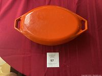 Photo of orange oval Dutch oven with lid on, showing top and handles.