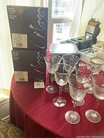 Photo showing 14 Mikasa Cristallo full lead crystal goblets on table next to two unopened boxes marked Mikasa Cristallo 14 goblets 4 pieces.