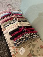 Photo of 18 assorted padded clothes hangers laid out side by side showing variety in fabric patterns and colors with metal hooks.