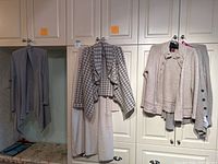 Five sweaters in neutral tones hanging on hooks and cabinets, showing various styles and textures