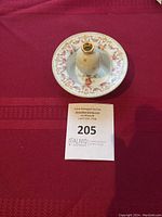 Top view of one Limoges petit dish showing the floral and gold decorative pattern with central vase on a red background beside auction lot tag.