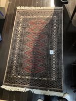 Top down photo of a rectangular printed Persian/Bokhara style rug with fringed ends on dark flooring.