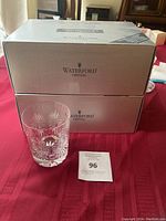Two Waterford Crystal boxes stacked behind one double old fashion glass on red tablecloth with auction lot card #96