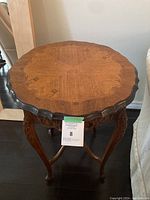 Photo of the entire antique style side table showing scalloped round top, carved legs, and curved supports