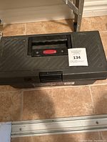 Closed black plastic toolbox with handle and latch on tile floor