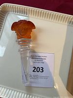 Front angle of frosted crystal bottle stopper with golden amber Medusa head topper sitting on auction lot card