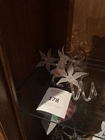 Set of six clear glass spiral flower decorations with frosted petals on a glass shelf.