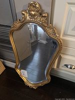 Front view of vintage gold coloured wall mirror showing ornate carved frame and mirror surface.