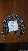 Full view of the necklace and earrings laid on a wooden surface with auction card showing lot number 75.