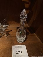 Full view of the vintage clear Waterford crystal decanter with stopper on wooden shelf, showing overall shape and label