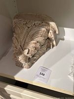 Carved wooden wall shelf with ornate leaf and scroll design in distressed white finish, placed on white surface.