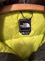Close-up of The North Face label inside black winter jacket showing small size and yellow lining.