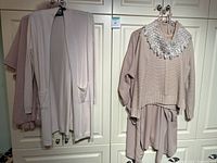 Multiple pink toned women's sweaters hanging on hangers against white closet doors.