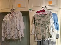 Several women's tops hanging on hangers showing variety of styles and colors, all summer styles with lace and light fabrics.