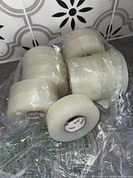 Twelve large rolls of clear packing tape wrapped in plastic.