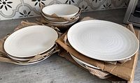 Photo showing stacks of white stoneware plates and bowls with cardboard separators on a kitchen counter.
